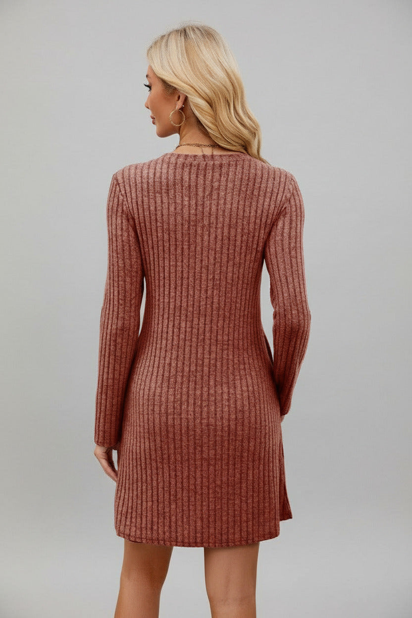 Woman wearing a brown ribbed dress standing in front of a white wall.