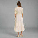 Woman wearing a white dress and sweater set against a beige background