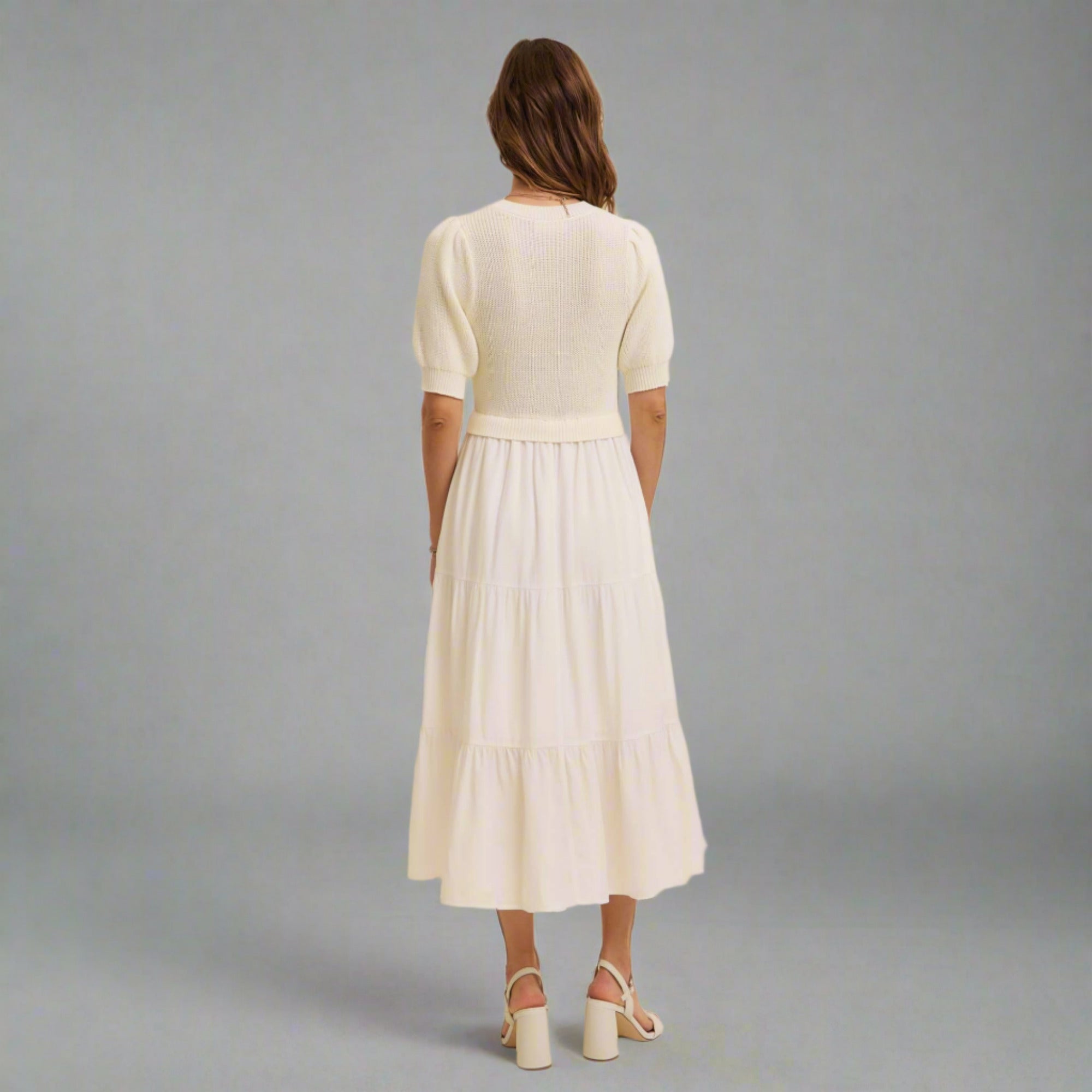 Woman wearing a white dress and sweater set against a beige background