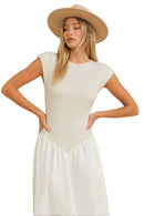 Woman wearing a beige top and white pants with a beige hat on a beige background