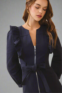 Navy blue dress with ruffled sleeves and a bow detail on a beige background