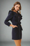 Woman wearing a navy blue dress with ruffled sleeves on a beige background