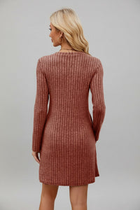 Woman wearing a brown ribbed dress standing in front of a white wall.