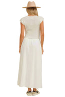 Woman wearing a white dress and beige hat against a beige background